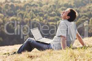 young man using laptop sitting on the grass on the hillside