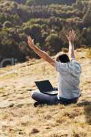 young man using laptop sitting on the grass on the hillside