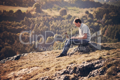 young man using laptop sitting on the grass on the hillside