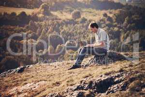 young man using laptop sitting on the grass on the hillside