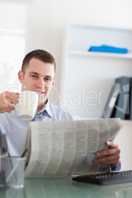 Smiling businessman reading the newspaper and having a coffee