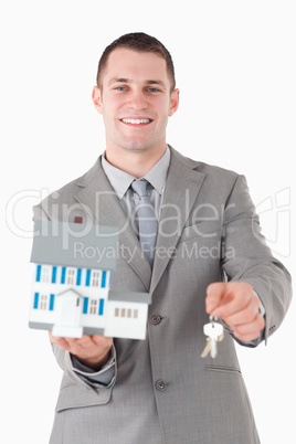 Portrait of a young businessman showing a miniature house and ke