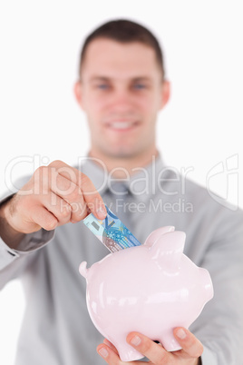 Portrait of a businessman putting a twenty euros note in a piggy