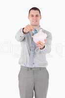Portrait of a businessman putting a note in a piggy bank