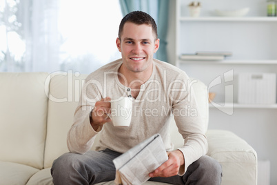 Man holding a newspaper while drinking a tea