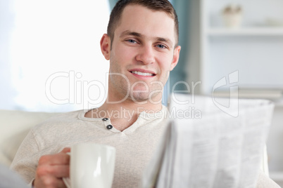 Smiling man having a tea while reading the news