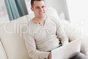 Smiling man using a laptop while sitting on a couch