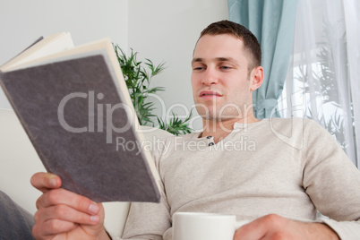 Man reading a book while holding a cup of tea