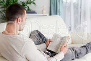 Portrait of a man lying on his couch reading a book