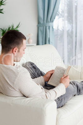 Portrait of a man lying on a sofa reading a book