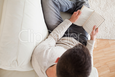 Man lying on a sofa reading a book