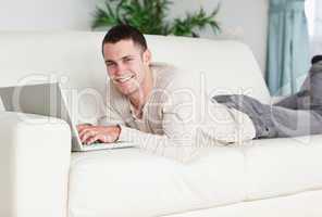 Smiling man lying on a sofa with a laptop