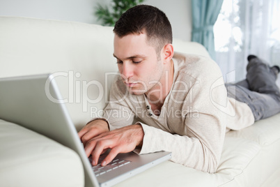 Focused man lying on a sofa using a laptop