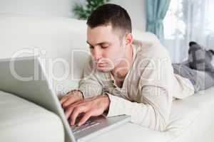 Focused man lying on a sofa using a laptop