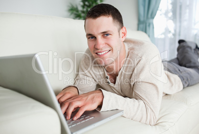 Smiling man lying on a couch with a laptop