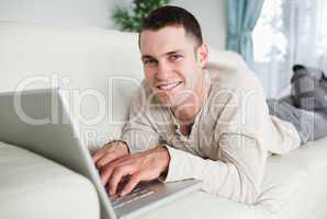 Smiling man lying on a couch with a laptop