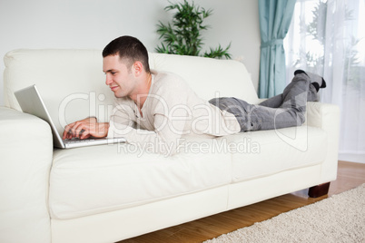 Handsome man lying on a couch using a notebook