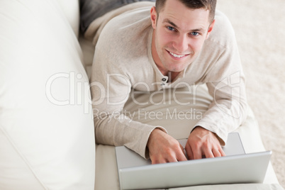 Happy man lying on a couch with a notebook