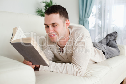 Young man lying on a couch to read a book