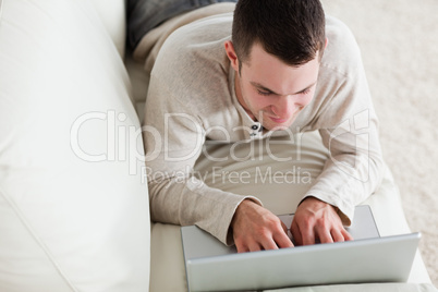 Young man lying on a couch to use a laptop