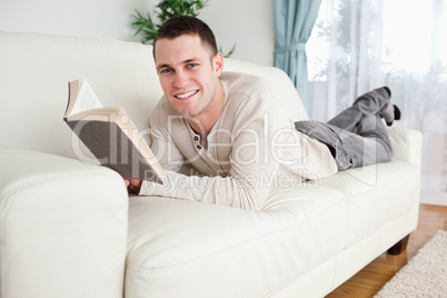 Young man lying on a couch reading a book