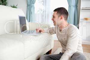 Smiling man sitting on a carpet while using a laptop