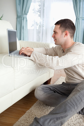 Portrait of a smiling man sitting on a carpet while using a lapt