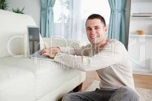 Smiling man sitting on a carpet with a laptop