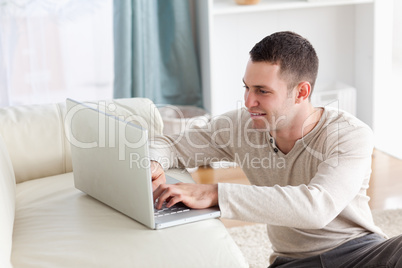 Smiling man sitting on a carpet while using a notebook