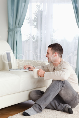 Portrait of a man sitting on a carpet using a laptop and holding