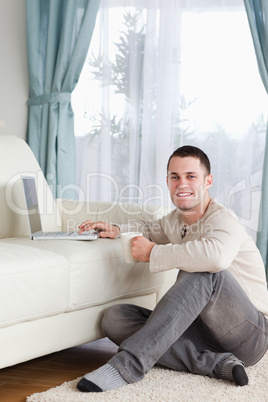 Portrait of a man sitting on a carpet with a cup of tea using a