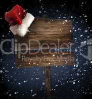 Wooden sign with santa hat on snowy background