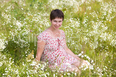 Cheerful pregnant woman sitting in chamomile