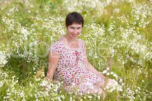 Cheerful pregnant woman sitting in chamomile