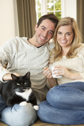 Young couple sitting with cat on sofa with cup in hand