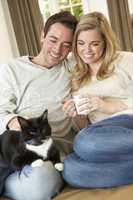 Young couple sitting with cat on sofa with cup in hand