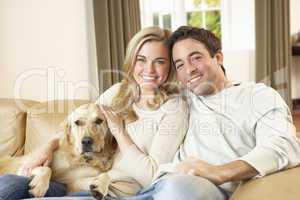 Young happy couple with dog sitting on sofa