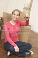 Young woman sits on the floor around boxes holding a key in her