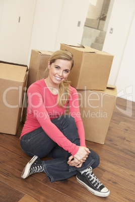 Young woman on moving day sitting on floor among cardboard boxes