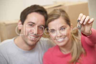 Young couple sit on the floor around boxes holding key in hand