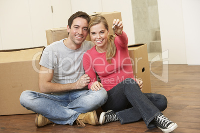 Young couple sit on the floor around boxes holding key in hand