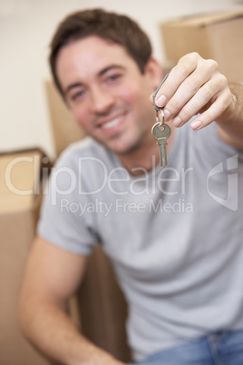 Young man sits on the floor around boxes holding a key in his ha