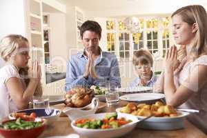 Family Saying Prayer Before Eating Roast Dinner