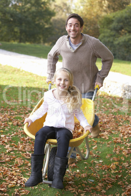 Father pushing child through autumn leaves on wheelbarrow