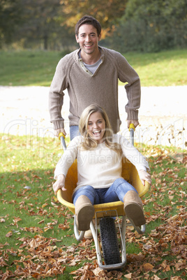 Man pushing wife through autumn leaves on wheelbarrow