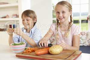 Happy children peeling vegetables in kitchen