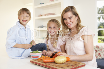 Young mother with children peeling vegetables in kitchen
