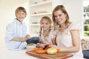 Young mother with children peeling vegetables in kitchen