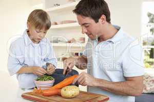 Happy young man with boy peeling vegetables in kitchen
