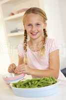Happy girl splitting peas in kitchen